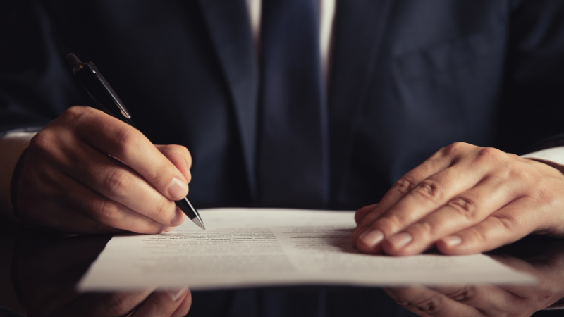  A business professional in a suit signing a contract, illustrating how contract finance is secured against the value of a signed agreement.